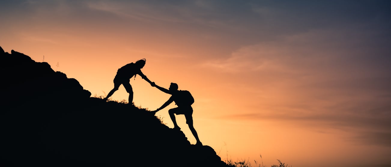 Two people helping each other climb up a mountain.